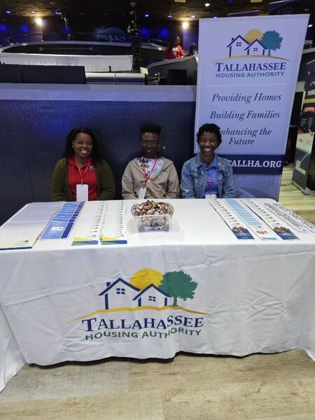 Three people from Tallahassee Housing Authority sitting at a tradeshow table with handouts and liturature on the table. 